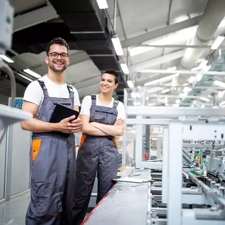 Bilden visar två personer som står i en fabrik