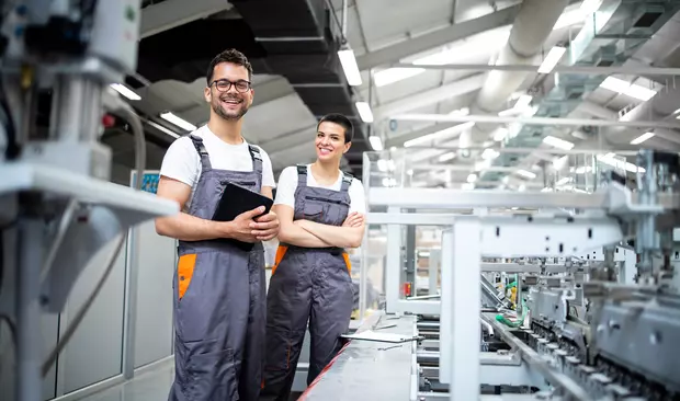 Bilden visar två personer som står i en fabrik