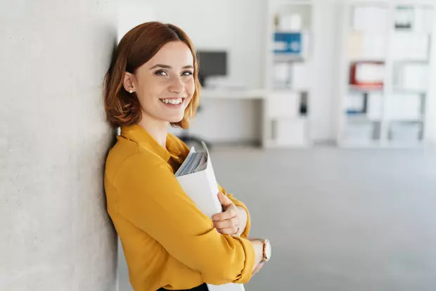 Bilden visar en kvinna på ett kontor med en pärm tryckt mot bröstet